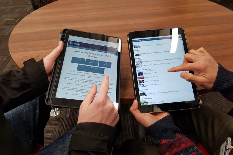 A photo from above of two people's hands looking at iPads