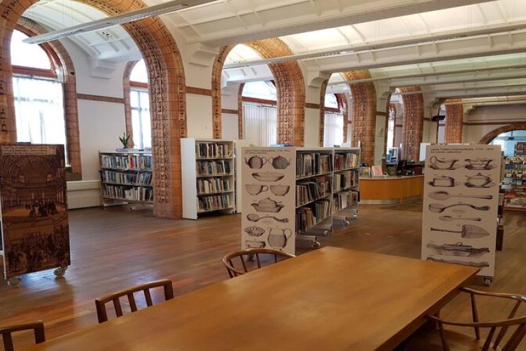 An internal shot of the Art Library with a long table, book shelves and books