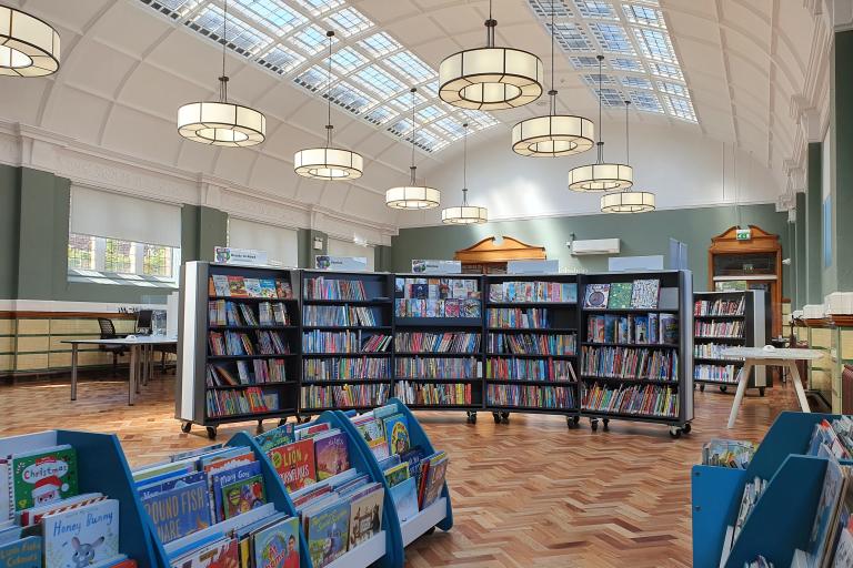 Internal photo of Armley Library with bookshelves, hanging lighting and wooden floor