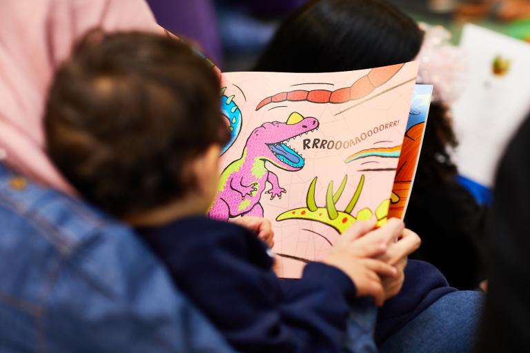 A photo from behind of a toddler reading a book