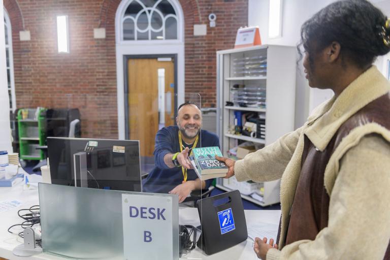 A lady handing books over at a library counter to a smiling staff member