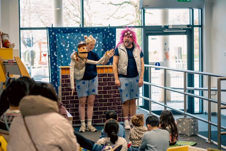 A man and a woman dressed up and acting on stage while a family audience watches
