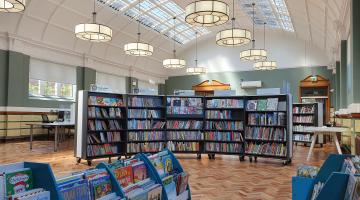 Internal photo of Armley Library with bookshelves, hanging lighting and wooden floor