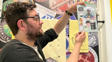 A man holding up a zine in front of a colourful display 