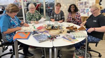 5 ladies sitting at a table working on a craft project