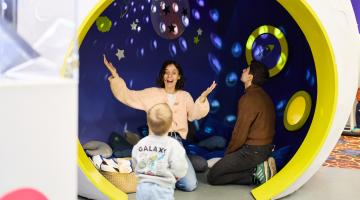 Two ladies and a child sitting inside an exhibition prop of a moon with projections